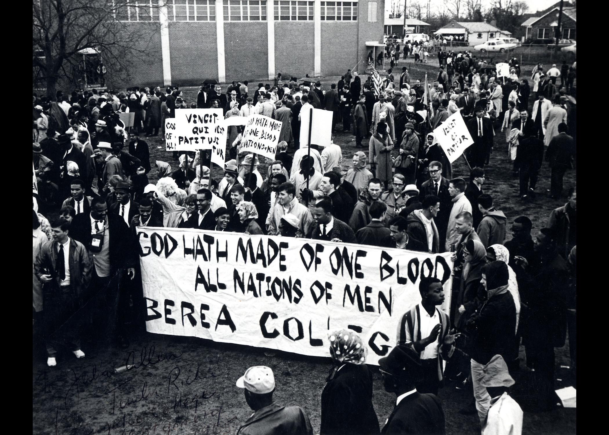 Black and white photo of Berea College students with a banner displaying the motto "God hath made of one blood all nations of men" before heading to the Selma march in 1965. Displaying the Berea College history.